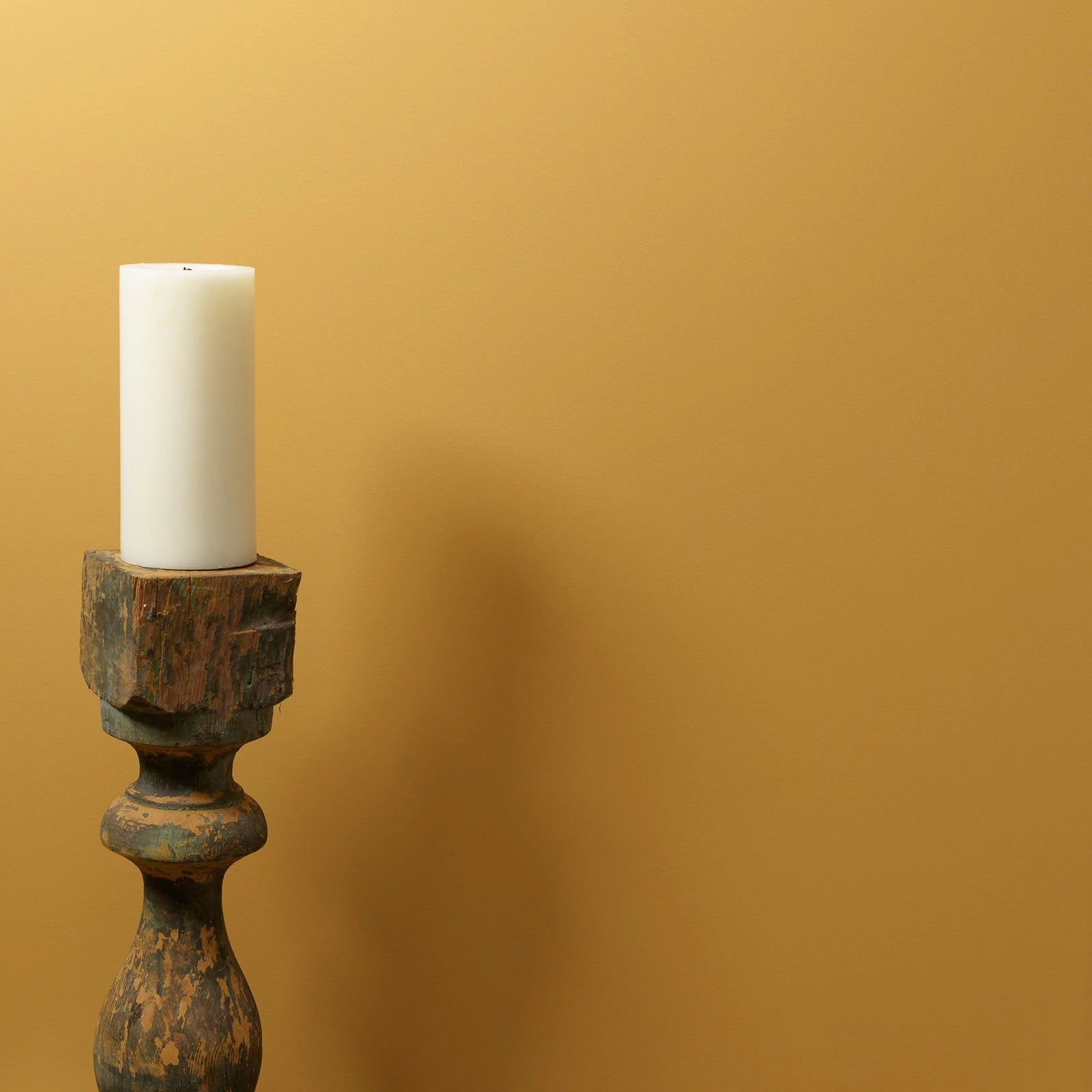 Luonnonhunajan värinen seinä, jonka edessä puinen kynttilänjälka ja valkoinen paksu kynttilä. 